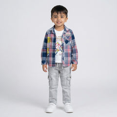 Young boy wearing a pink and blue checked shirt over a white graphic t-shirt with light grey cargo jeans and white sneakers against a light studio background