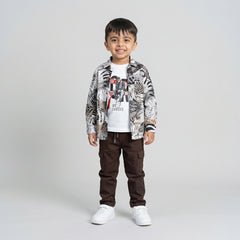 Young boy wearing a tropical print shirt over a white graphic t-shirt with brown cargo pants and white sneakers against a light studio background