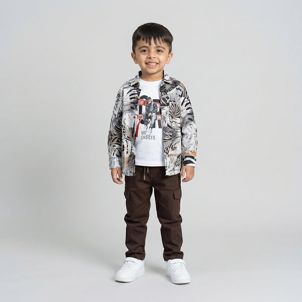 Young boy wearing a tropical print shirt over a white graphic t-shirt with brown cargo pants and white sneakers against a light studio background