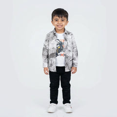 Young boy smiling in a printed casual shirt, white graphic T-shirt, black pants, and white sneakers, standing against a plain light background.