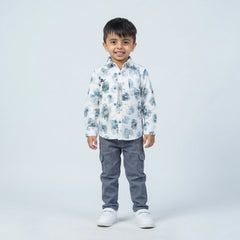 Young boy wearing a white printed full sleeve shirt, grey cargo pants, and white sneakers, standing and smiling against a plain light background.