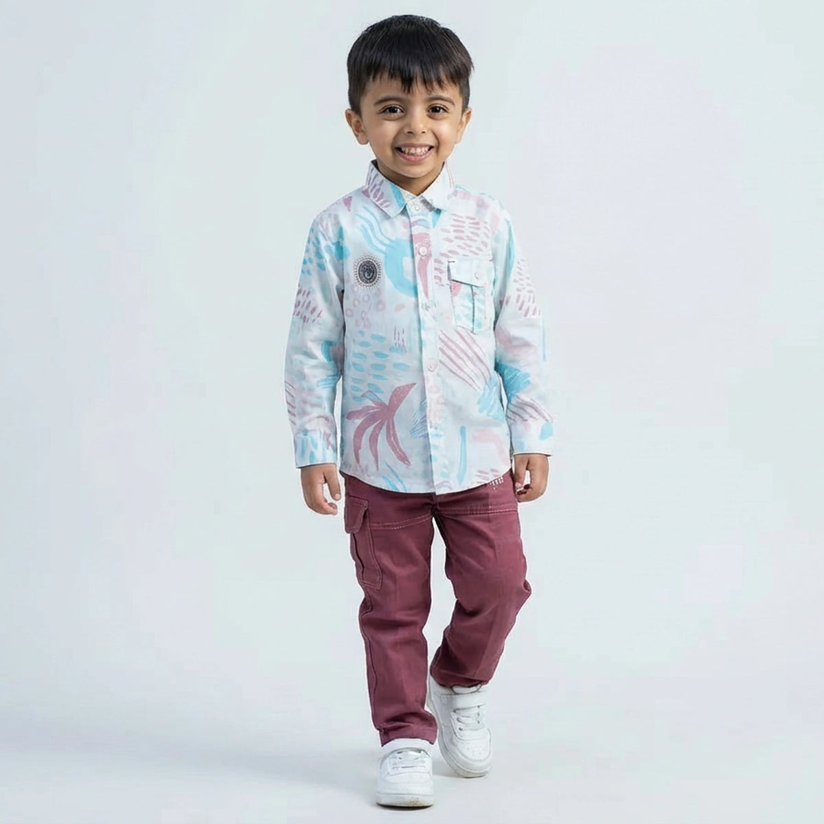Young boy wearing an abstract print casual shirt with cargo pants and white sneakers, shown in pink color  against a plain light background