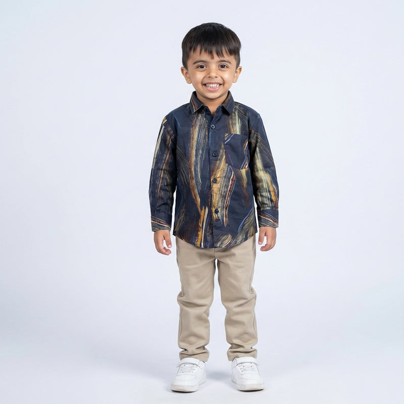 Young boy smiling in a navy abstract printed full sleeve shirt, beige pants, and white sneakers, standing against a plain light background.
