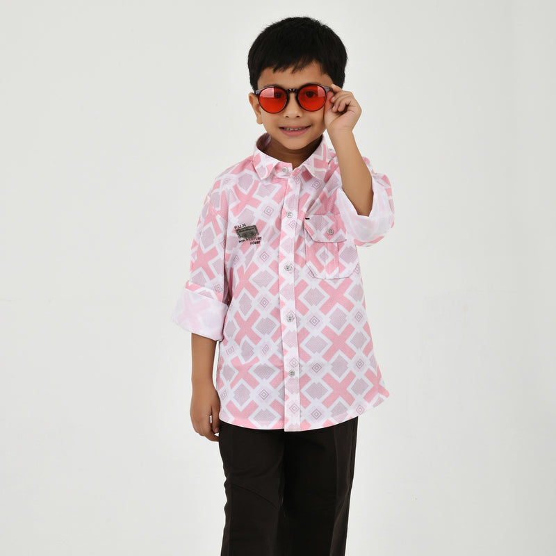 Young boy wearing a geometric print casual shirt with dark pants and white sneakers, shown in pink and green color variants against a plain light background.
