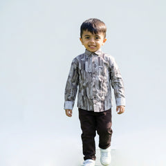 Young boy wearing a grey camouflage print full sleeve shirt, dark pants, and white sneakers, walking and smiling against a plain light background.