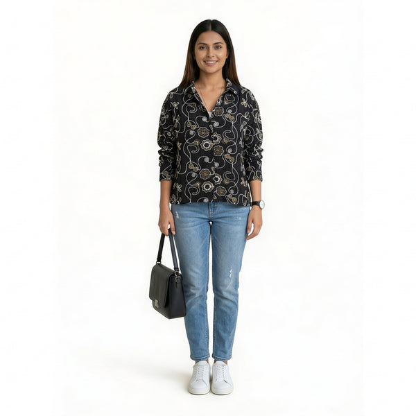 A woman wearing a black printed button-down shirt with floral swirl patterns, paired with light blue slim-fit jeans, white sneakers, and a black shoulder bag.

