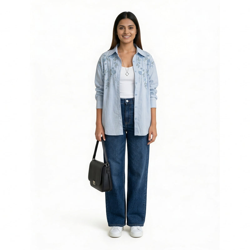 A woman wearing a light blue embroidered button-down shirt over a white top, paired with dark blue straight-leg jeans, white sneakers, and carrying a black shoulder bag.