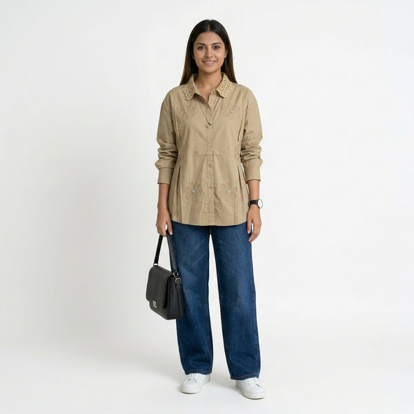 A woman wearing a beige button-down shirt with floral embroidery and a textured collar, paired with blue straight-leg jeans and white sneakers, holding a structured black handbag.