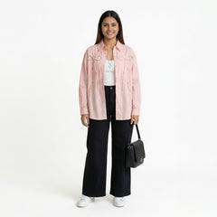 A smiling woman wearing a light pink button-down shirt with bow detailing, layered over a white top, paired with black wide-leg jeans and white sneakers, holding a structured black handbag.