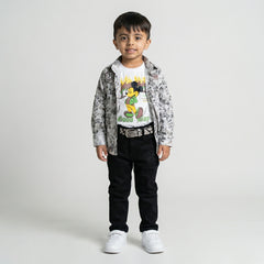 Young boy wearing a grey printed shirt over a white graphic t-shirt with black trousers, belt, and white sneakers against a light studio background