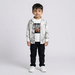 Young boy wearing a grey printed shirt over a white graphic t-shirt with black cargo pants and white sneakers against a light studio background