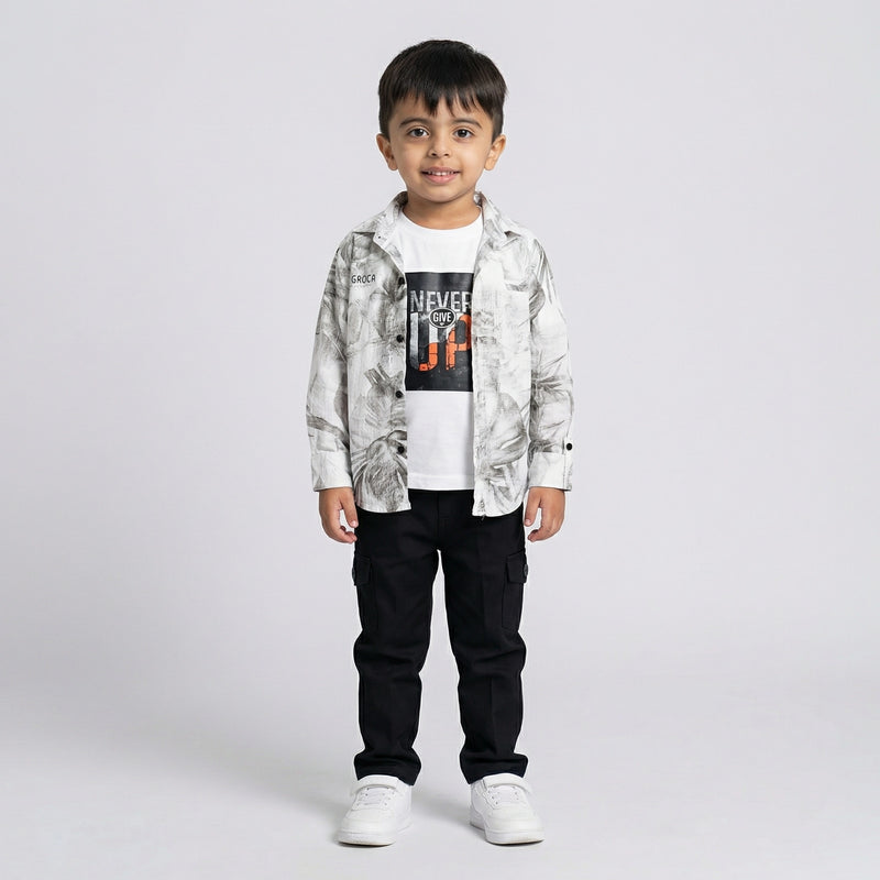 Young boy wearing a grey printed shirt over a white graphic t-shirt with black cargo pants and white sneakers against a light studio background