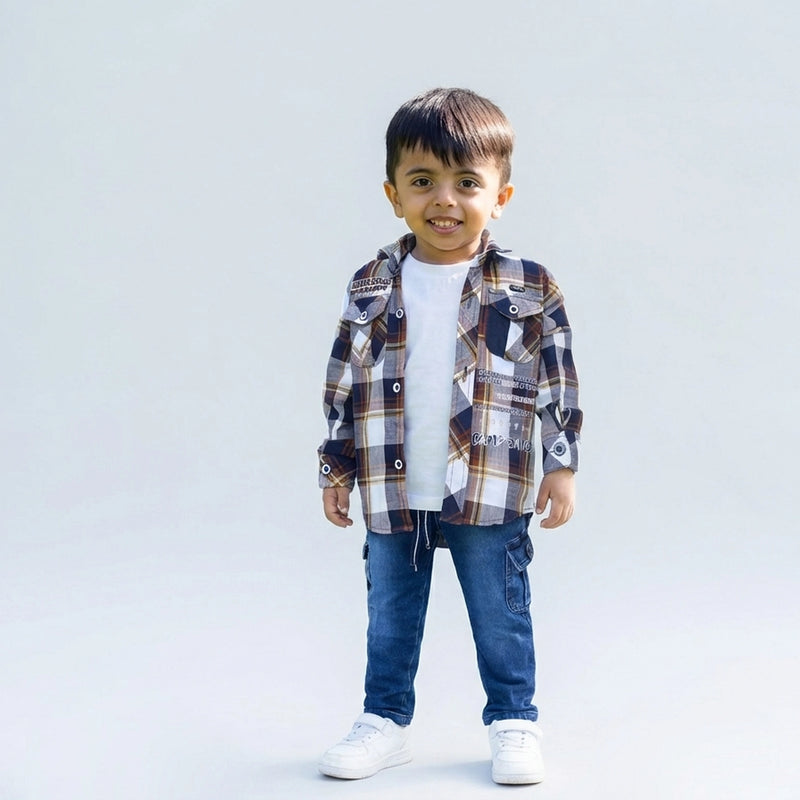 Young boy smiling in a brown checked casual shirt over a white T-shirt, blue cargo jeans, and white sneakers, standing against a plain light background.