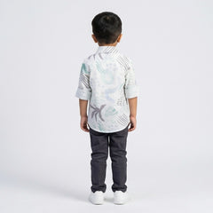 Young boy wearing an abstract print casual shirt with cargo pants and white sneakers, shown in green color against a plain light background.