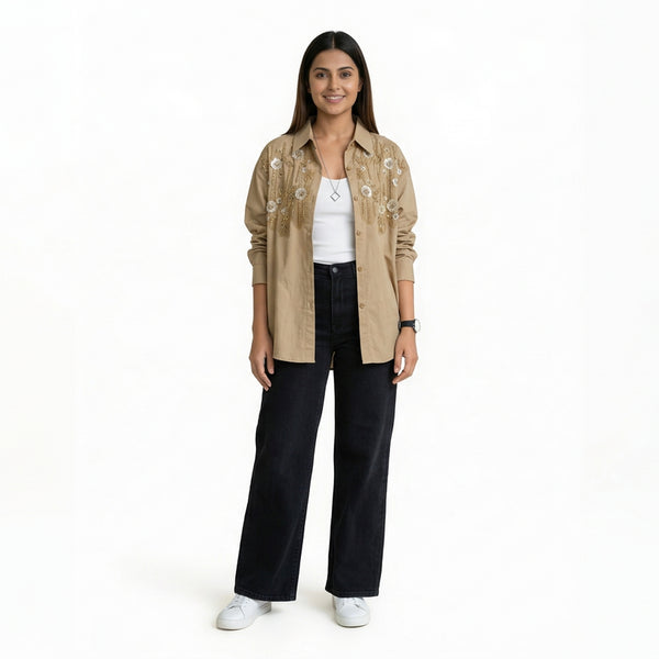 A woman wearing a beige embroidered button-down shirt over a white top, paired with black wide-leg jeans and white