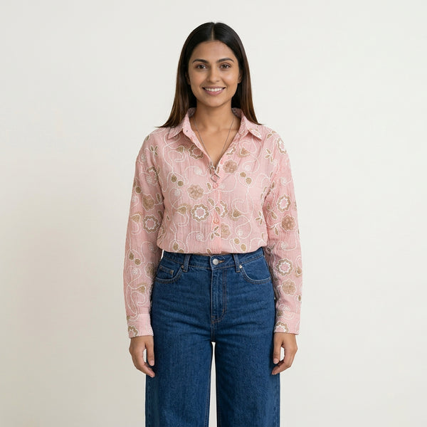 A woman wearing a pink floral printed button-down shirt tucked into high-waisted blue jeans, styled with a minimal necklace, against a plain background.