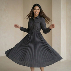 Woman wearing a charcoal grey shirt-style dress with a cinched waist and pleated skirt, twirling in a minimal indoor setting.

