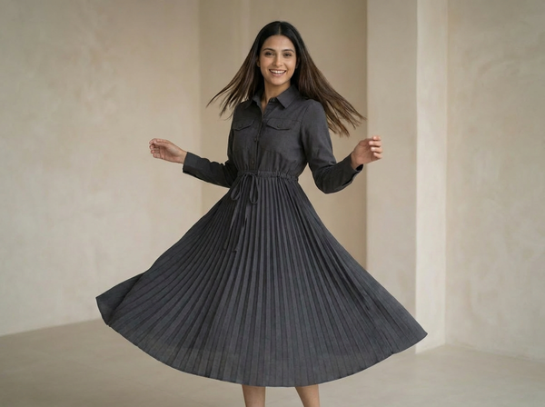 Woman wearing a charcoal grey shirt-style dress with a cinched waist and pleated skirt, twirling in a minimal indoor setting.


