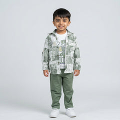 Young boy wearing a sage green printed shirt over a white graphic t-shirt with matching green pants and white sneakers against a light studio background