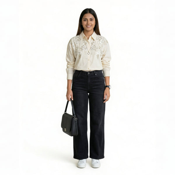 A woman wearing a cream embroidered button-down shirt paired with black straight-leg jeans, white sneakers, and carrying a black shoulder bag.

