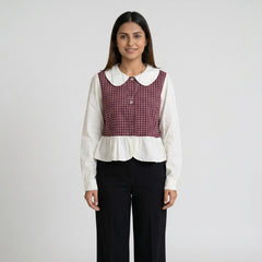 Woman wearing a white blouse with a red plaid vest on a gray background