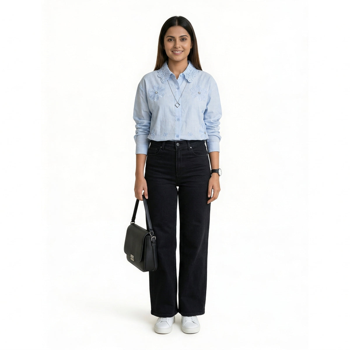 A woman wearing a light blue button-down shirt with floral embroidery and a textured collar, paired with black straight-leg jeans and white sneakers, holding a structured black handbag.