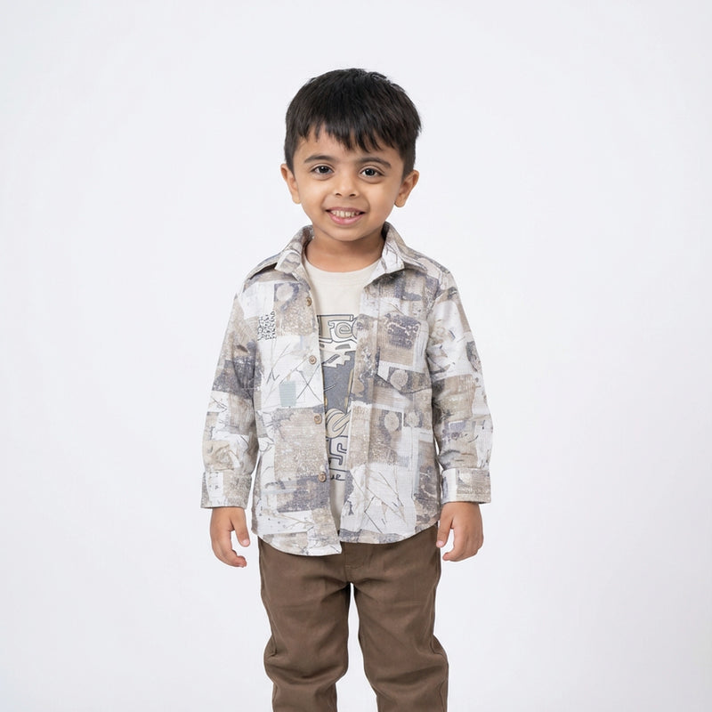 Young boy wearing a beige printed shirt over a graphic t-shirt with brown casual pants against a light studio background