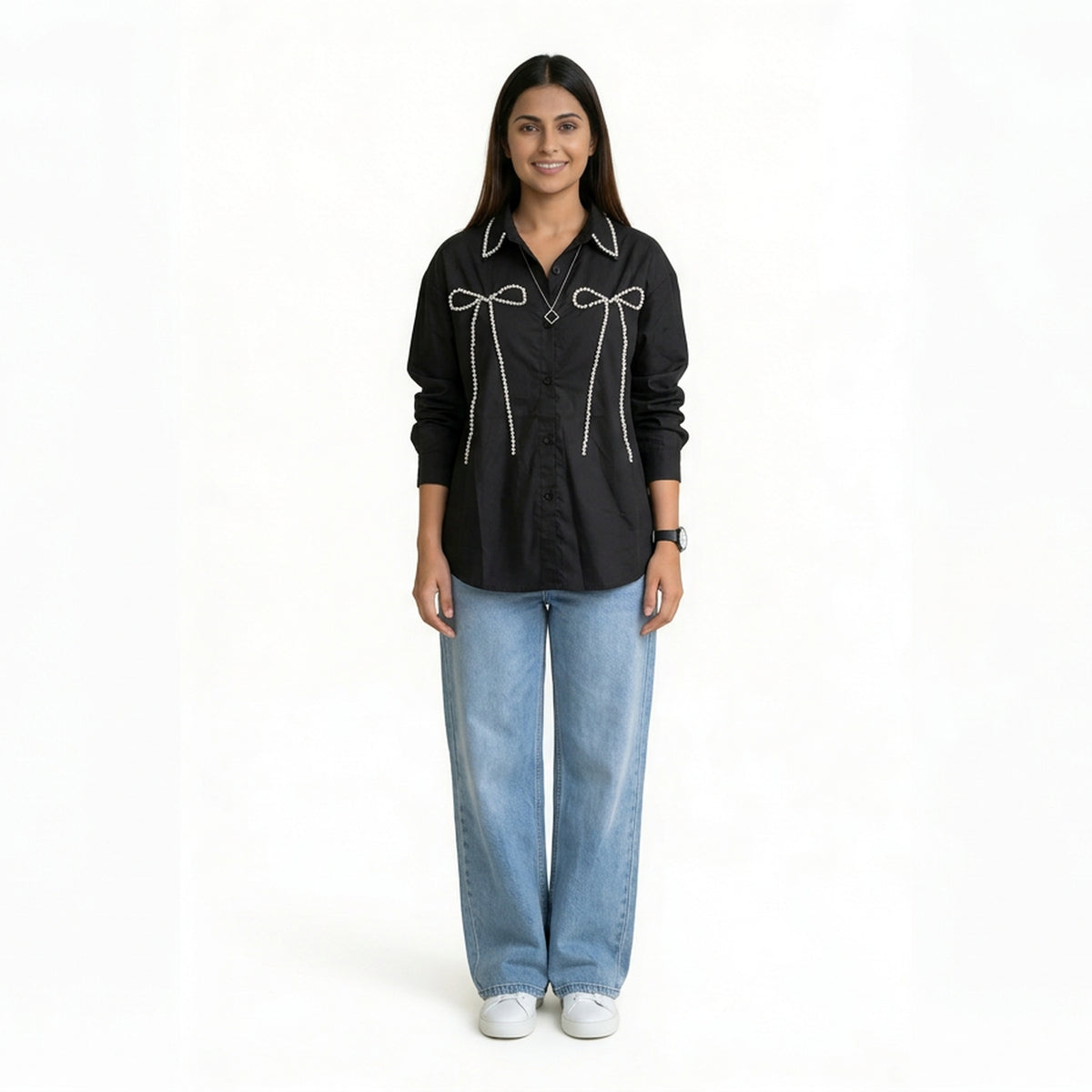 A woman wearing a black button-down shirt with bow embellishment details on the front, paired with light blue wide-leg jeans and white sneakers.