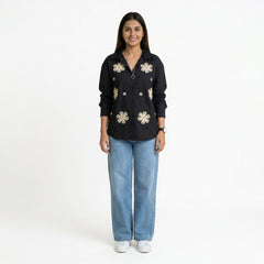 A woman wearing a black button-down shirt with floral embroidery, paired with light blue straight-leg jeans and white sneakers.