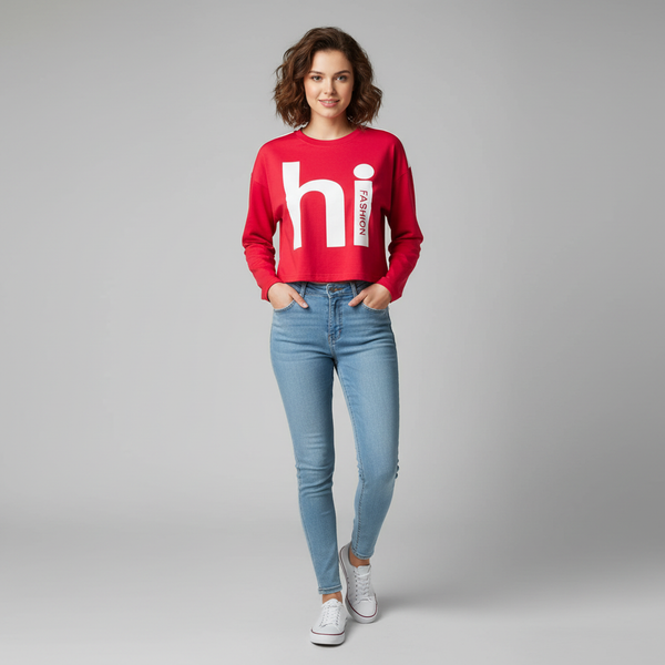 Woman wearing a red cropped sweatshirt with “hi fashion” graphic print, paired with light blue skinny jeans and white sneakers, posing against a plain grey background.

