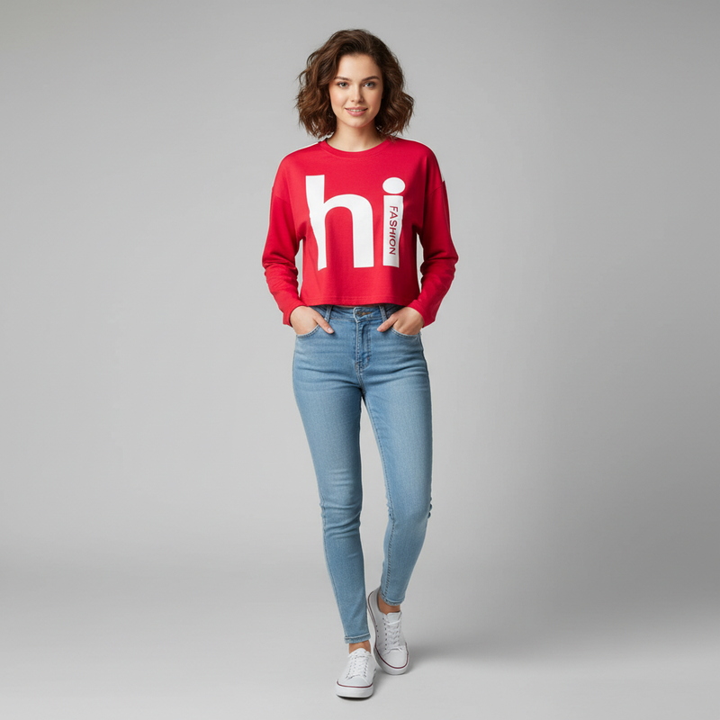 Woman wearing a red cropped sweatshirt with “hi fashion” graphic print, paired with light blue skinny jeans and white sneakers, posing against a plain grey background.

