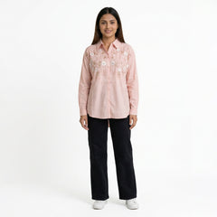 A woman wearing a pink embroidered button-down shirt paired with black straight-leg jeans and white sneakers.