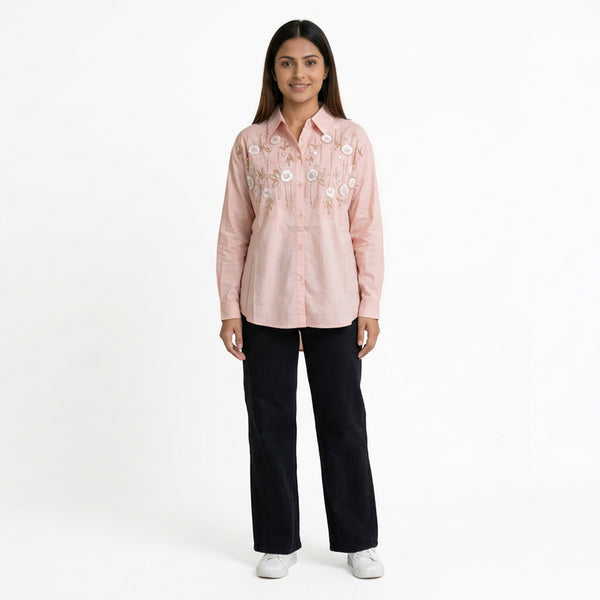 A woman wearing a pink embroidered button-down shirt paired with black straight-leg jeans and white sneakers.