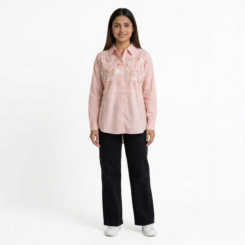 A woman wearing a pink embroidered button-down shirt paired with black straight-leg jeans and white sneakers.