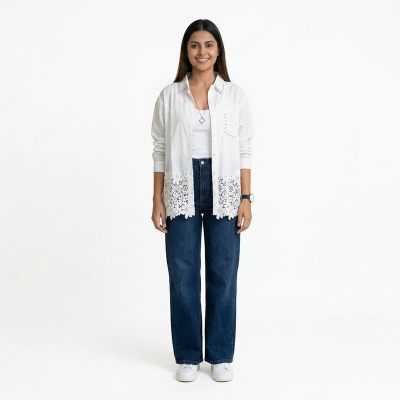 A smiling woman wearing a white button-down shirt with lace detailing at the hem and stud accents, layered over a white top, paired with blue wide-leg jeans and white sneakers.