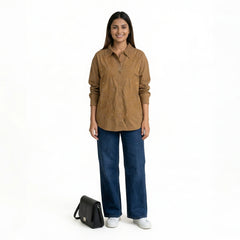 A woman wearing a brown button-down shirt with intricate embroidered detailing and a textured collar, paired with blue wide-leg jeans and white sneakers, with a black handbag placed beside h