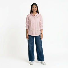 A woman wearing a light pink button-down shirt with floral embroidery, paired with blue wide-leg jeans and white sneakers.