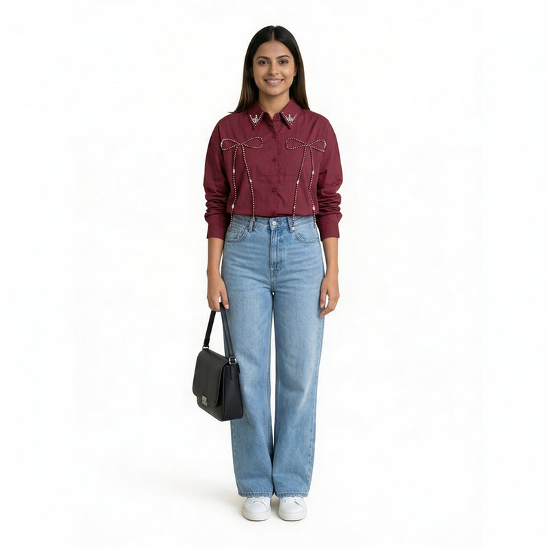 A woman wearing a maroon button-down shirt with bow embellishment details on the front, paired with light blue straight-le