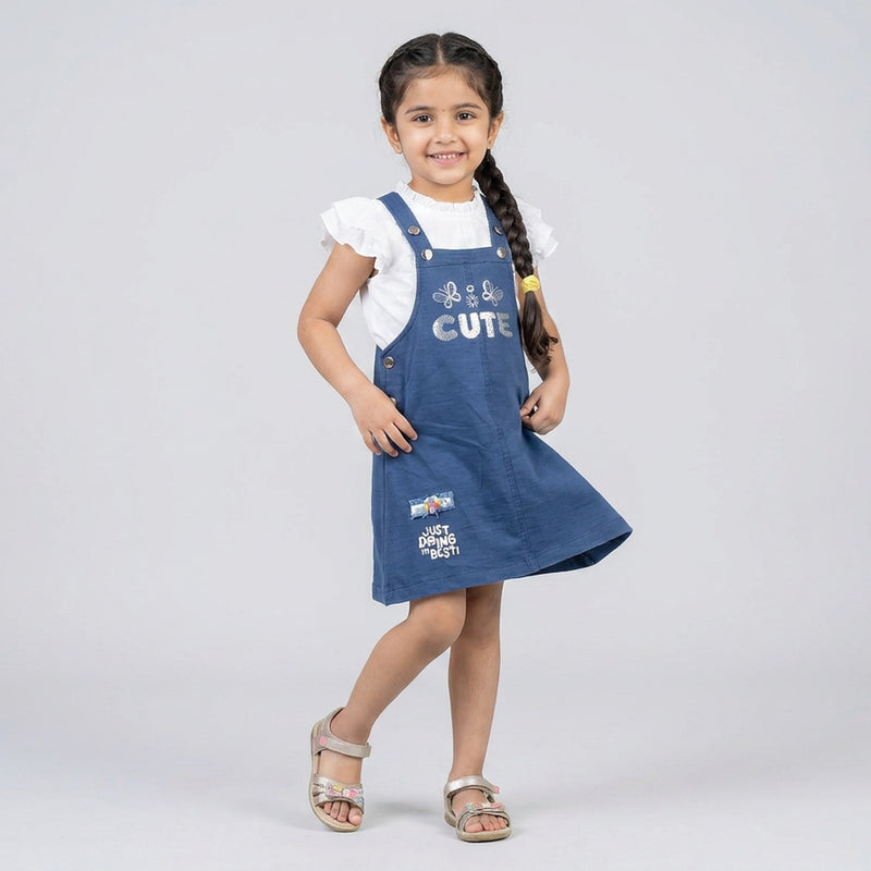 Girl wearing blue pinafore dress with white ruffle sleeve top cute kids casual outfit dungaree style dress for girls