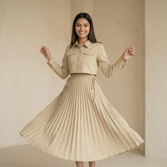 Woman wearing a beige cropped shirt paired with a matching pleated midi skirt, twirling in a minimal indoor setting.

