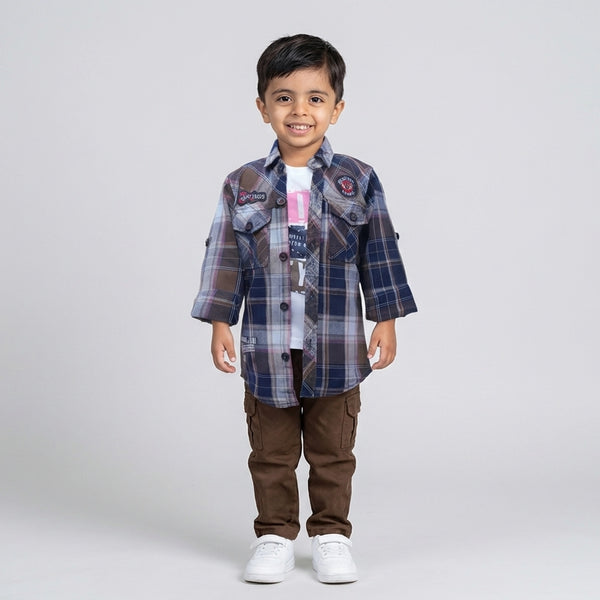 Boy dressed in a blue and brown checked shirt, white graphic t-shirt, brown cargo pants, and white sneakers in a studio photoshoot