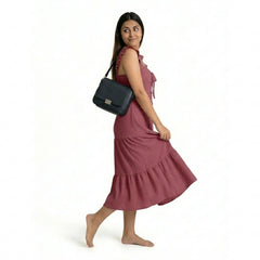 A woman wearing a sleeveless maroon midi dress with ruffled straps and a tiered, textured skirt, walking barefoot while carrying a black shoulder bag.