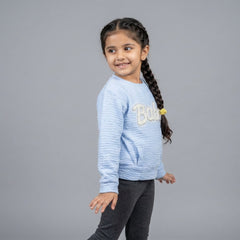 Young girl wearing a light blue sweater with 'Bella' on it against a gray background