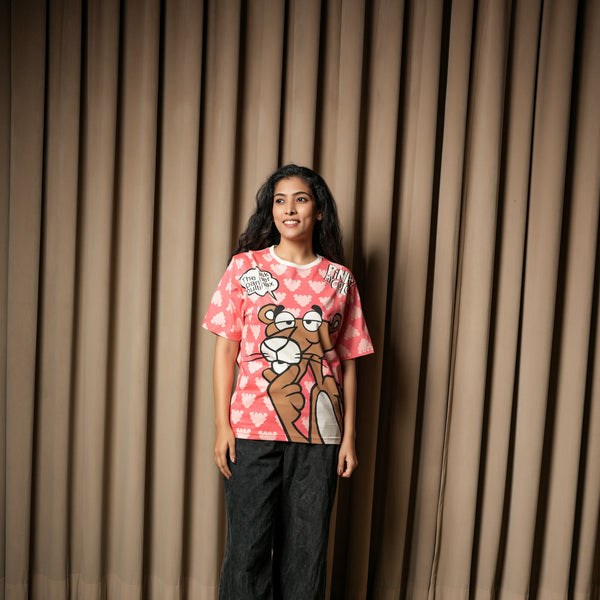 A woman wearing a pink graphic T-shirt with a Pink Panther print, paired with dark jeans, standing against a curtain

