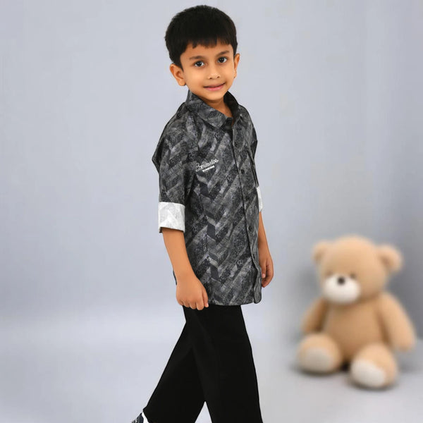 Child wearing a patterned shirt and black pants with a teddy bear in the background