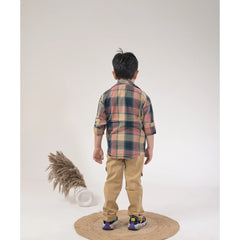 Boy dressed in a brown checked shirt, white graphic t-shirt, khaki cargo pants, and white sneakers in a studio photoshoot