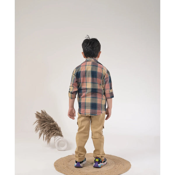 Boy dressed in a brown checked shirt, white graphic t-shirt, khaki cargo pants, and white sneakers in a studio photoshoot