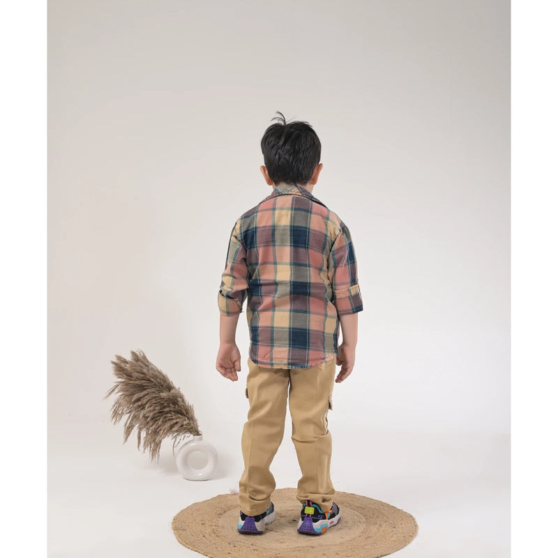 Boy dressed in a brown checked shirt, white graphic t-shirt, khaki cargo pants, and white sneakers in a studio photoshoot