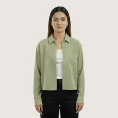 Woman wearing a light green shirt over a white inner and black pants on a beige background