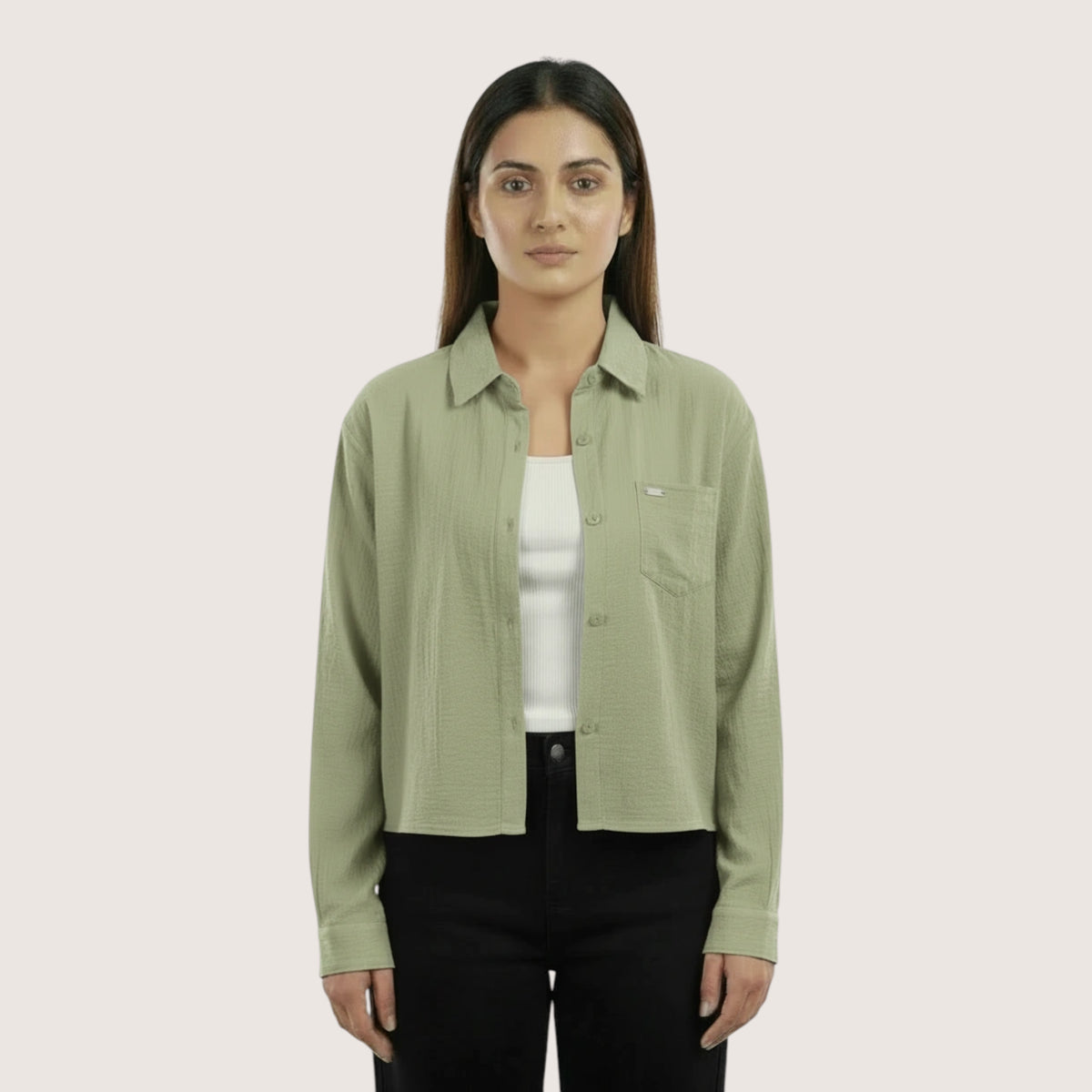 Woman wearing a light green shirt over a white inner and black pants on a beige background